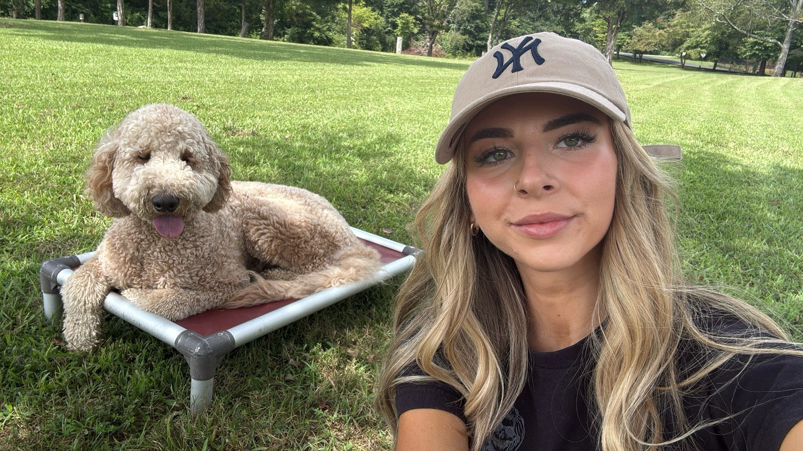 A trainer taking a selfie with a curly goldendoodle resting on a raised bed